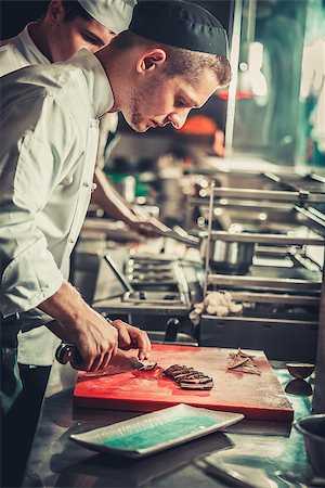 Food concept. Young serious chef in white uniform cut beef steak meat dish on red cutting board in interior of modern professional restaurant kitchen. Ready to serve. Ready to eat Stock Photo - Budget Royalty-Free & Subscription, Code: 400-09028537