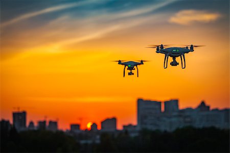 Two drone quad copters with high resolution digital camera flying aerial over spectacular sunset orange sky. Cityscape silhouette with sun goes down in the background.Vehicle at sundown and copy space Photographie de stock - Aubaine LD & Abonnement, Code: 400-09029158
