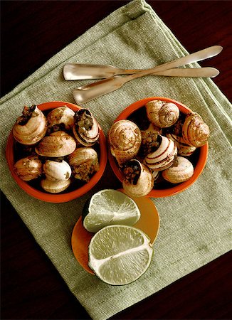 escargot - Two Bowls of Delicious Escargot with Garlic Butter, Silver Forks and Sliced Lime closeup on Green Napkin. Top View Stock Photo - Budget Royalty-Free & Subscription, Code: 400-09063766