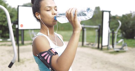simsearch:400-04969467,k - Beautiful ethnic woman in sportswear using smartphone and headphones and drinking water with eyes closed in park. Photographie de stock - Aubaine LD & Abonnement, Code: 400-09112293