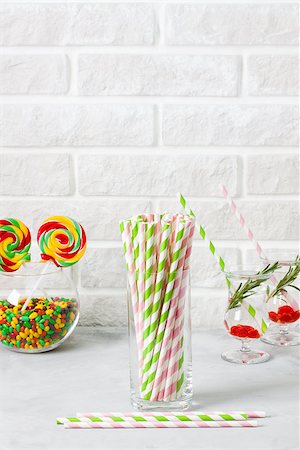 Glass with striped green and pink drinking straws and colored candies and lolipops in a glass round jar on  white painted brick wall background with vertical copyspace for advertasing, invitation, greeting Stock Photo - Budget Royalty-Free & Subscription, Code: 400-09170489