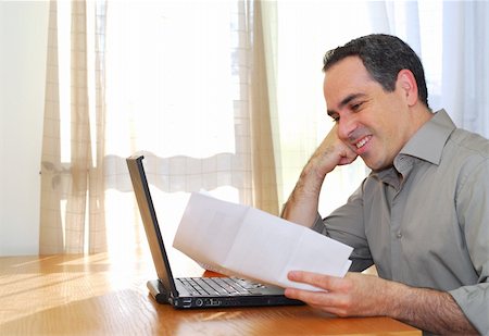 face card - Man sitting at his desk with a laptop and papers looking happy Photographie de stock - Aubaine LD & Abonnement, Code: 400-03915227