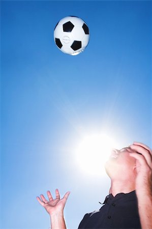 A male soccer referee or coach catching a soccer ball. He is wearing a black shirt and the sun is shining from behind his face. There is movement on his hands and the ball but elements of the face is sharp. Stock Photo - Budget Royalty-Free & Subscription, Code: 400-03924808