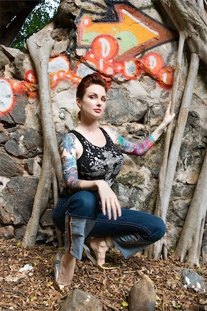 simsearch:400-04450827,k - Sexy Caucasian tattooed woman crouching next to wall covered in graffiti and Banyan tree branches. Stock Photo - Budget Royalty-Free & Subscription, Code: 400-03925208