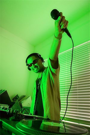 Smiling Asian young adult male DJ wearing sunglasses and holding microphone up in front of mixing equipment and turntable. Stock Photo - Budget Royalty-Free & Subscription, Code: 400-03921202