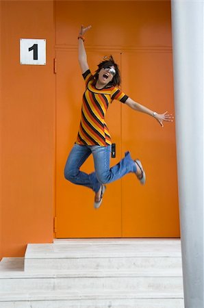 Cosmopolitan girl jumping of happiness in front of a orange building Stock Photo - Budget Royalty-Free & Subscription, Code: 400-03934247