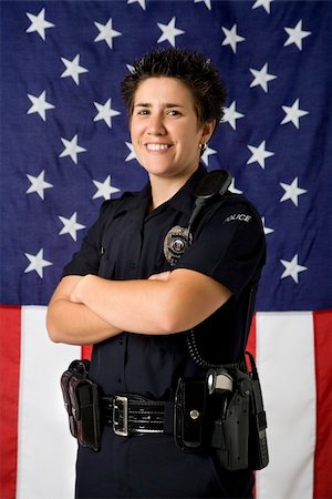 female police officer happy - Portrait of mid adult Caucasian policewoman standing with arms crossed with American flag as backdrop smiling at viewer. Photographie de stock - Aubaine LD & Abonnement, Code: 400-03940755