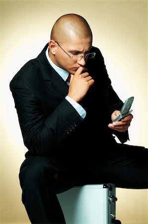 simsearch:400-03954954,k - A businessman wearing black suit, using cell phone and sitting on case Stock Photo - Budget Royalty-Free & Subscription, Code: 400-03955071