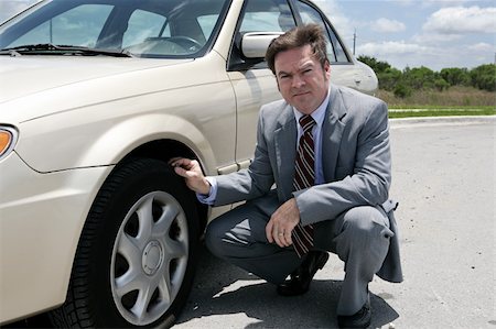 An unhappy looking businessman discovering a screw in his flat tire. Stock Photo - Budget Royalty-Free & Subscription, Code: 400-03972282