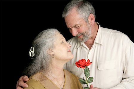 A beautiful mature woman receiving a red rose from her loving husband.  Focus on wife.  Black background Stock Photo - Budget Royalty-Free & Subscription, Code: 400-03972903