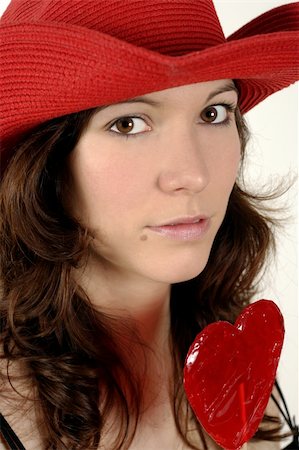 Image of a beautiful young woman wearing a red cowboy and holding a heart-shaped lollipop. Stock Photo - Budget Royalty-Free & Subscription, Code: 400-03985658