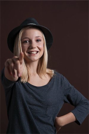 simsearch:600-03456225,k - Portrait of Blond, Teenage Girl, Smiling at Camera, wearing Hat and Pointing finger, Studio Shot on Black Background Stock Photo - Premium Royalty-Free, Code: 600-06438954