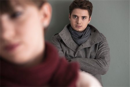 Portrait of Young Man Standing behind Young Woman, Looking at her Intensely, Studio Shot on Grey Background Foto de stock - Sin royalties Premium, Código: 600-06486264