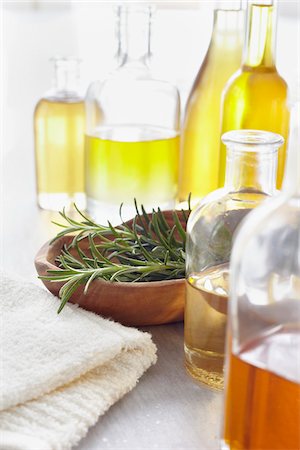 Sprig of rosemary in a bowl, fresh herbs, a towel and bottles of essential oil for aromatherapy Stock Photo - Premium Royalty-Free, Code: 600-06675021