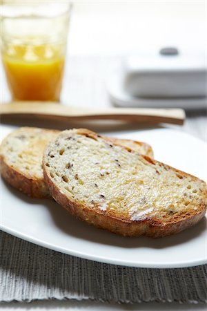 Close-up of Buttered Multigrain Toast with Wooden Knife and Glass of Orange Juice, Studio Shot Stock Photo - Premium Royalty-Free, Code: 600-06773341