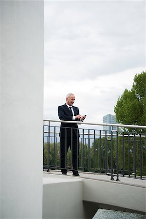Mature businessman standing on bridge, looking at smartphone, Mannheim, Germany Stock Photo - Premium Royalty-Free, Code: 600-06782218