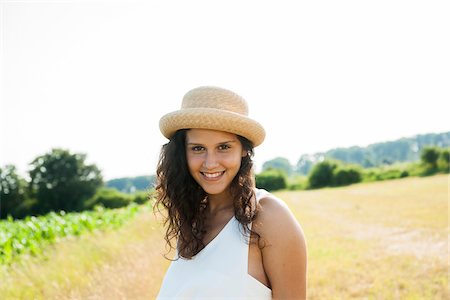 simsearch:700-07148202,k - Portrait of teenaged girl standing in field, wearing straw hat, smiling at camera, Germany Photographie de stock - Premium Libres de Droits, Code: 600-06899843