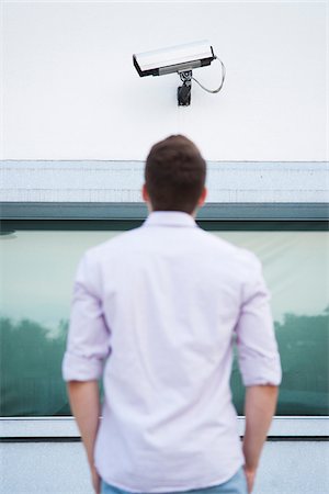 Backview of young man standing outdoors, looking at security camera, Germany Stock Photo - Premium Royalty-Free, Code: 600-06899934