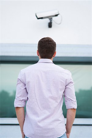 Backview of young man standing outdoors, looking at security camera, Germany Stock Photo - Premium Royalty-Free, Code: 600-06899935