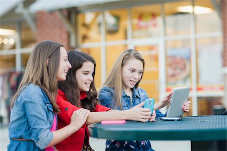 photos of mixed race teenage girls - Girls using Cell Phone and Tablet Computer at Outdoor Cafe, USA Stock Photo - Premium Royalty-Free, Code: 600-06892610