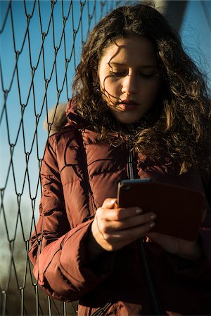 simsearch:600-03244230,k - Close-up of teenage girl standing next to chain link fence, wearing winter coat and using smart phone, Germany Stock Photo - Premium Royalty-Free, Code: 600-07311005