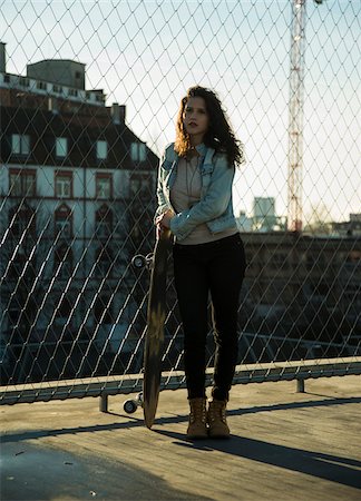 simsearch:600-06786785,k - Teenage girl standing outdoors next to chain link fence near comercial dock, holding skateboard, Germany Stock Photo - Premium Royalty-Free, Code: 600-07311001