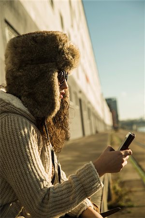 simsearch:600-07567389,k - Close-up of teenage girl outdoors, wearing trapper hat and sunglasses, sitting next to building at loading dock, looking at smart phone, Mannheim, Germany Stock Photo - Premium Royalty-Free, Code: 600-07311096