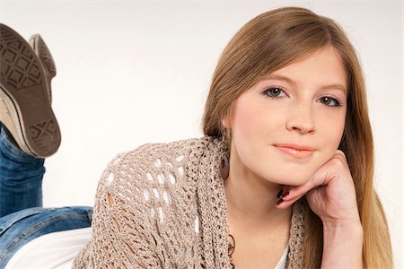 female wearing trainers - Close-up portrait of young, blond, long-haired woman lying on stomach, looking at camera and smiling, studio shot on white background Stock Photo - Premium Royalty-Free, Code: 600-07348153