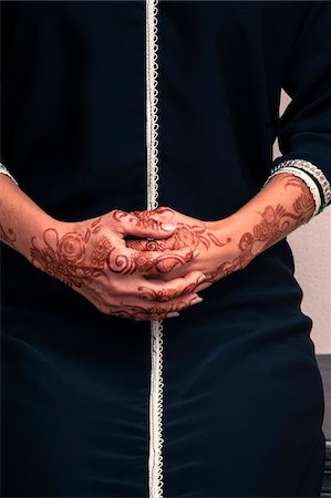 Woman sitting indoors with close-up of folded hands painted with henna in arabic style, wearing a typical black, arabic, muslim dress, studio shot Stock Photo - Premium Royalty-Free, Code: 600-07434935