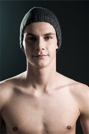 Close-up portrait of young man wearing toque, looking at camera, studio shot on black background Stock Photo - Premium Royalty-Free, Code: 600-07567378