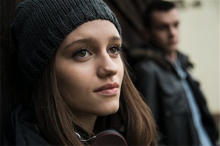 Close-up portrait of teenage girl outdoors, wearing hat and headphones around neck, with young man in background, Germany Photographie de stock - Premium Libres de Droits, Code: 600-07567384