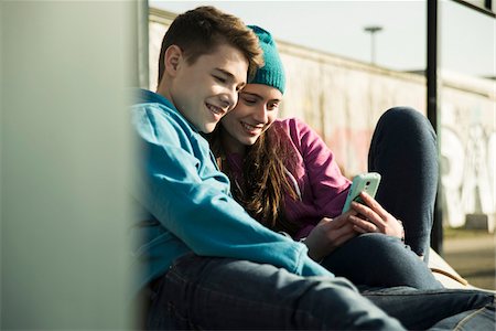 simsearch:600-06786785,k - Teenage girl and boy sitting on ground, smiling and looking at cell phone together, Mannheim, Germany Stock Photo - Premium Royalty-Free, Code: 600-07584764