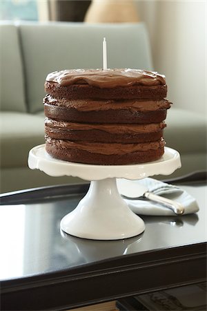 simsearch:600-02461257,k - Layered Chocolate Birthday Cake with Candle on Cake Stand on Coffee Table Stock Photo - Premium Royalty-Free, Code: 600-08274203