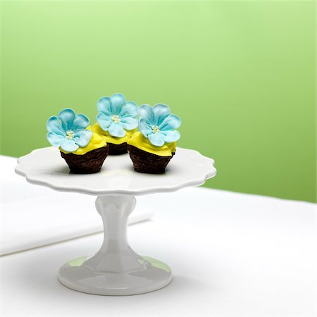 Chocolate Cupcakes with Yellow Icing and Blue Sugar Flowers on Cake Stand Stock Photo - Premium Royalty-Free, Code: 600-08512619