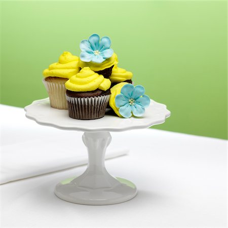 chocolate and vanilla cupcakes with yellow icing and blue sugar flowers on a cake stand Stock Photo - Premium Royalty-Free, Code: 600-08512621