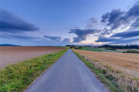 simsearch:600-08169205,k - Countryside with harvested cereal field and paved laneway at dusk in summer at Roellbach in Spessart hills in Bavaria, Germany Stock Photo - Premium Royalty-Free, Code: 600-08973333