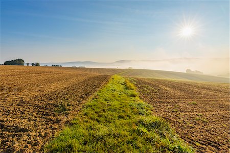 simsearch:600-06334488,k - Countryside with grassy pathway through plowed fields with the sun and morning mist in autumn in the village of Schmachtenberg in Bavaria, Germany Stock Photo - Premium Royalty-Free, Code: 600-08973363