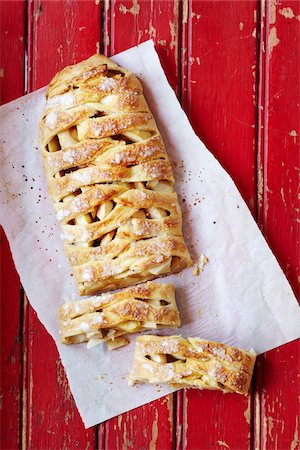 section - Apple strudel on parchment paper with two slices cut off on a red barnboard surface Stock Photo - Premium Royalty-Free, Code: 600-09119389