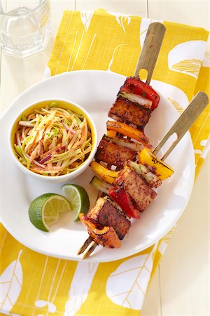 simsearch:600-06892689,k - Grilled tofu and bell peppers on bamboo skewers with side dish of slaw and lime wedges on a yellow patterned napkin Stock Photo - Premium Royalty-Free, Code: 600-09119404