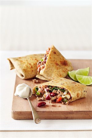 spoonful - Bean Burrito stuffed with ground beef, peppers and lettuce, on wooden cutting board with a spoon of sour cream Stock Photo - Premium Royalty-Free, Code: 600-09119427