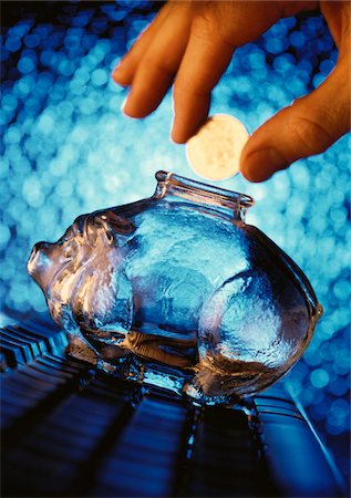 Hand Putting Coin into Glass Piggy Bank Stock Photo - Premium Royalty-Free, Code: 600-00056360