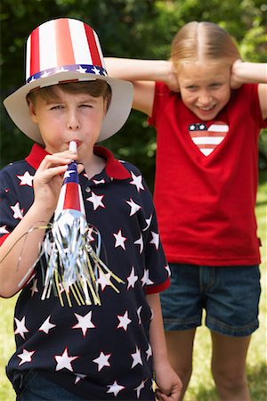 Portrait of Boy Wearing Stars and Stripes Top and Hat, Blowing Noisemaker Horn, Girl Watching Stock Photo - Premium Royalty-Free, Code: 600-01041997