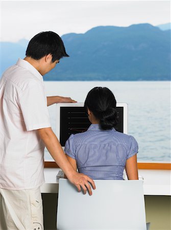 Man and Woman Looking at Computer in Front of Window with Ocean View Stock Photo - Premium Royalty-Free, Code: 600-01124836