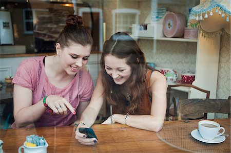 Young women in cafe looking at cell phone Stock Photo - Premium Royalty-Free, Code: 614-05662150