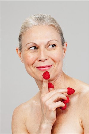 Mature woman wearing raspberries on fingertips, smiling Stock Photo - Premium Royalty-Free, Code: 614-06002261