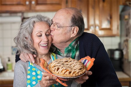Senior man kissing woman holding freshly baked pie Stock Photo - Premium Royalty-Free, Code: 614-06044613