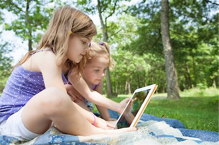 Two girls sitting on picnic blanket with digital tablet Foto de stock - Sin royalties Premium, Código: 614-06336320