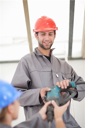 Male and female laborer handing electric drill on construction site Stock Photo - Premium Royalty-Free, Code: 614-06814009