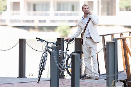 Young man by chain fence with bicycle on cell phone Stock Photo - Premium Royalty-Free, Code: 614-06813821