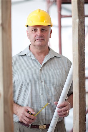 Portrait of a builder with tape measure and blueprint on construction site Stock Photo - Premium Royalty-Free, Code: 614-06813853